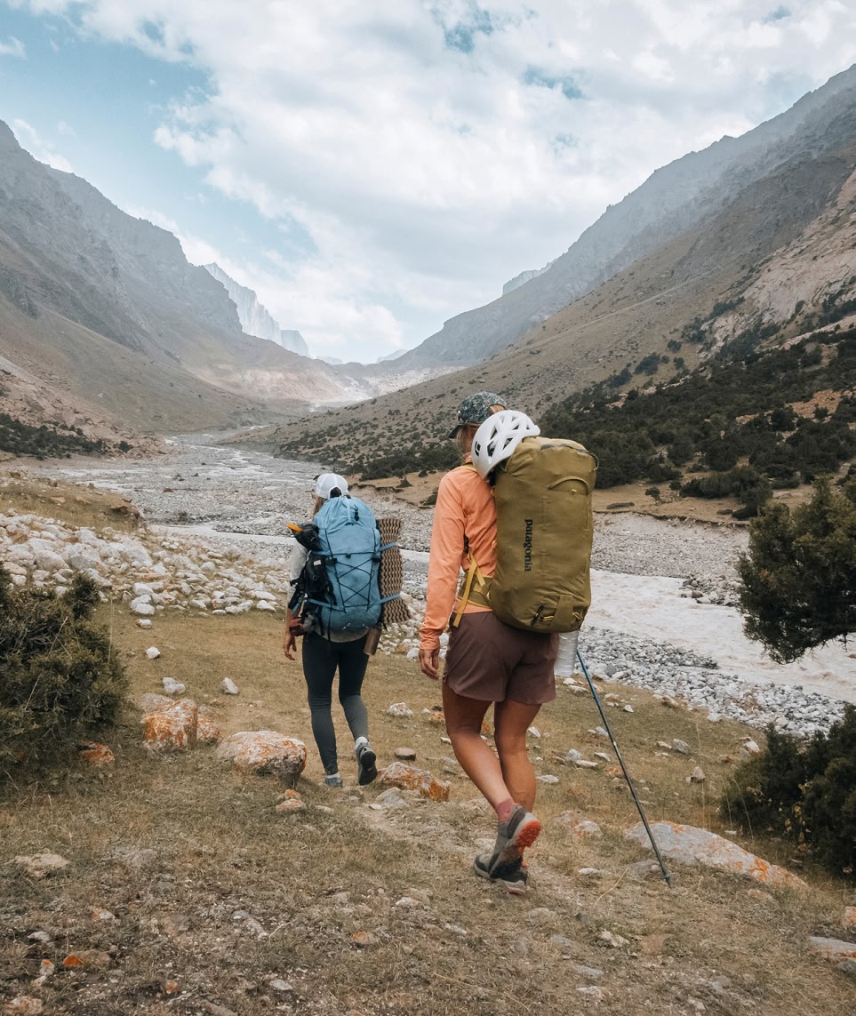 Two climbers with large backpacks trek through a remote river valley.