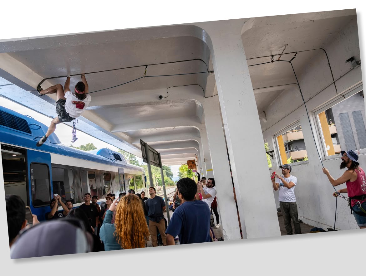 A climber hangs upside down from a crack in the outside roof of a train station.