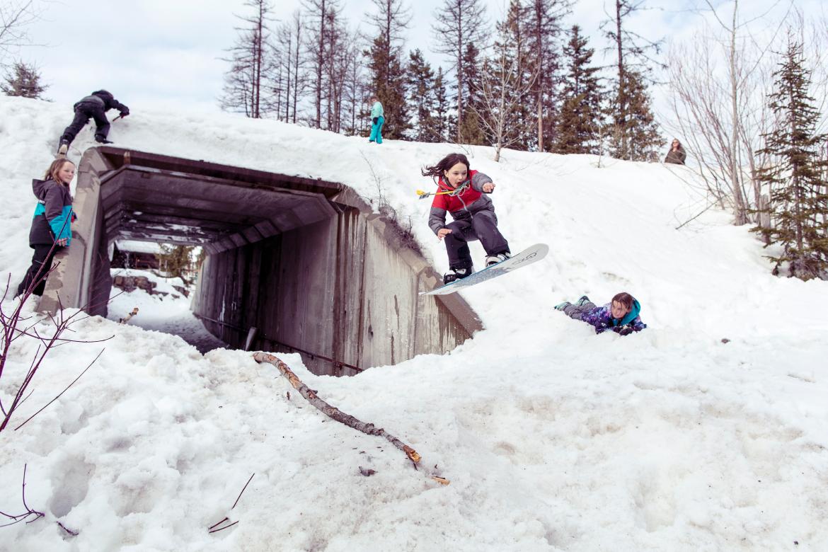 A kid snowboards through a tunnel and hits a jump.