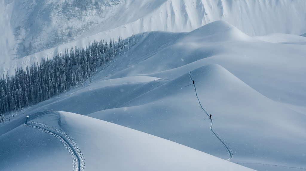 Two people hike up a steep, snowy hill on skis.