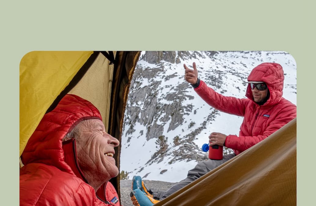 Two people sit and talk at a high-altitude campsite.    