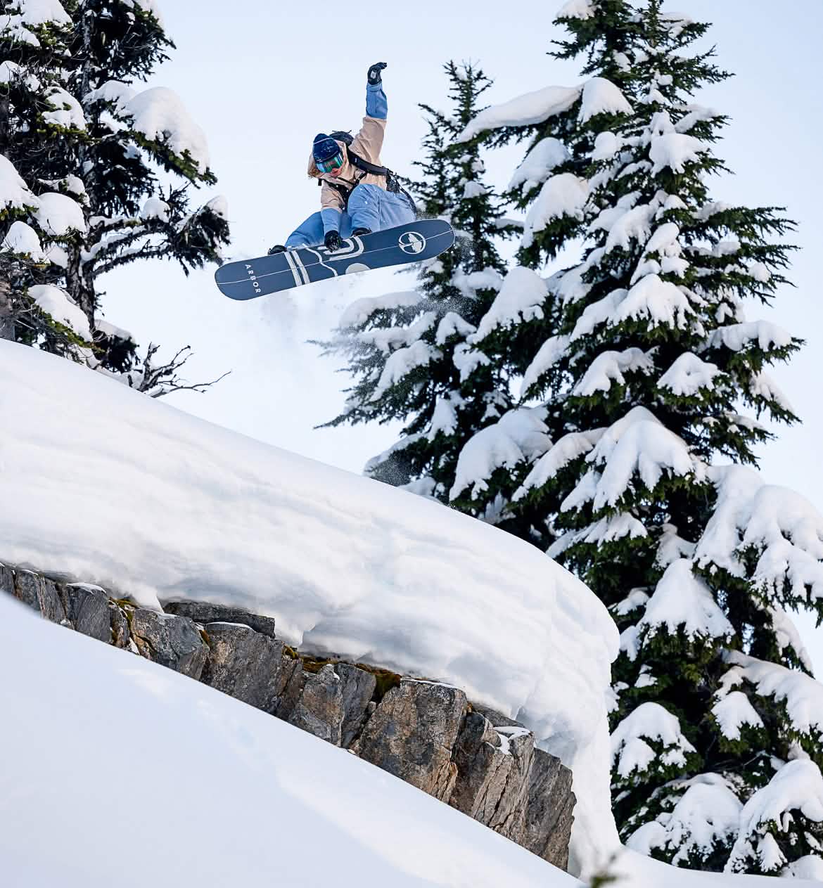 A snowboarder catches air over a snow-covered rock.
