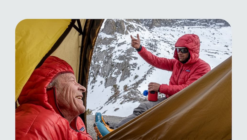 A climber peers out of the tent at their partner in the mountains. 
