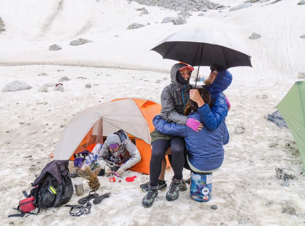Three hikers gather under one umbrella during a storm.