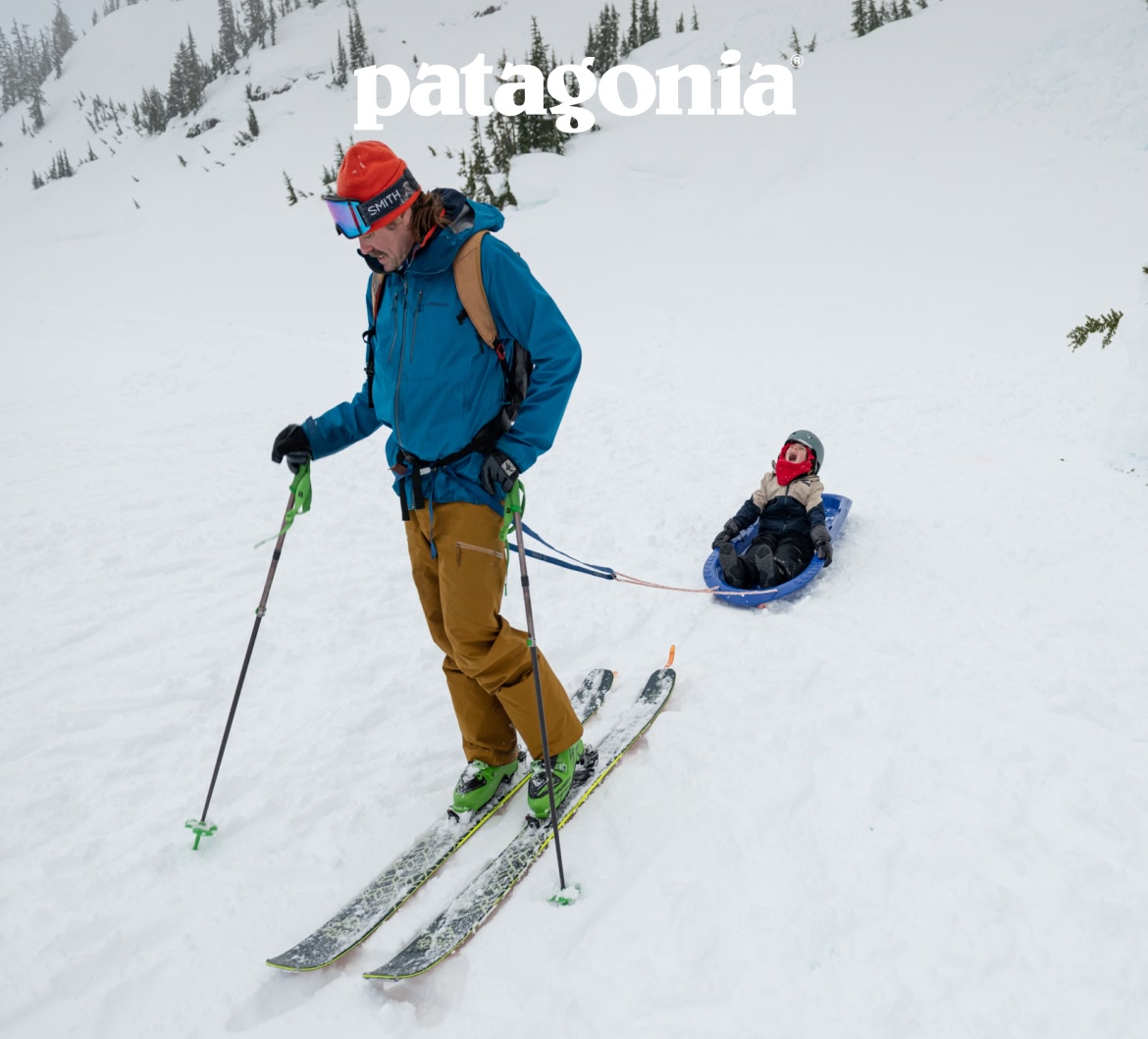 A dad on skis tows his son in a sled behind him.