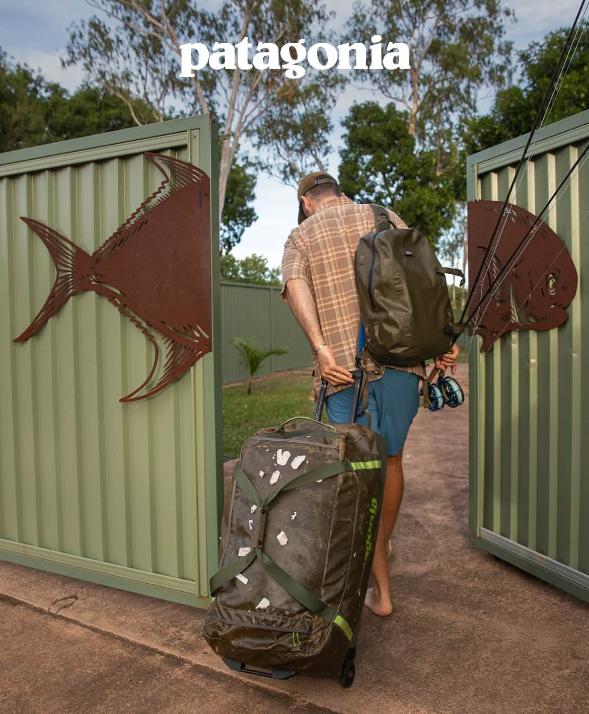 Patagonia. A person holding two fly rods pulls luggage past a gate with a large fish depicted on it.
