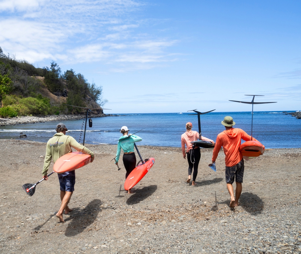 Four people with hyrofoils walk into the ocean.