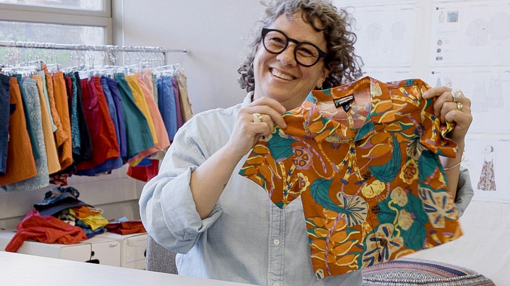 A smiling person holds a child’s shirt with a tropical print.