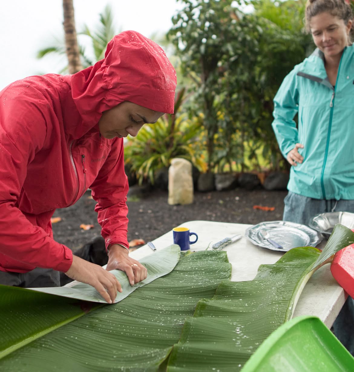 Two people prepare dinner outside in tropical rain.