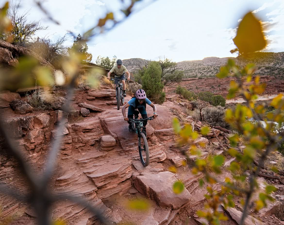 Two people riding bikes down a rock. 