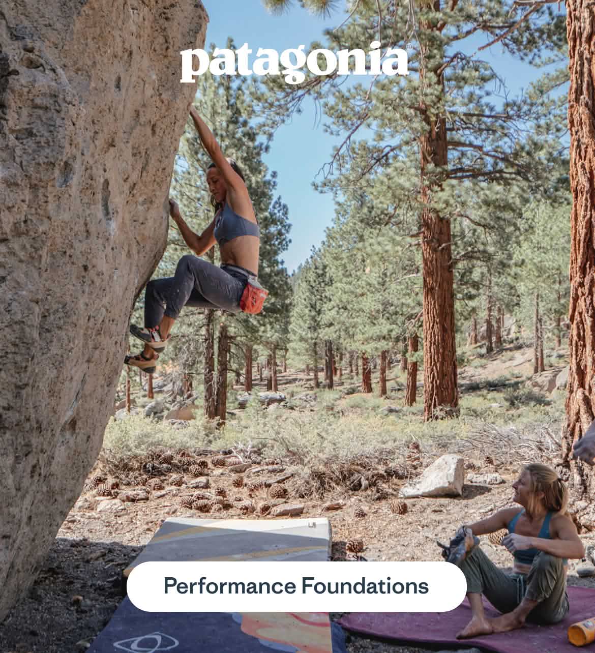 A women in a sports bra and joggers climbs a boulder  in an open forest while her friends sit at the base, smiling.