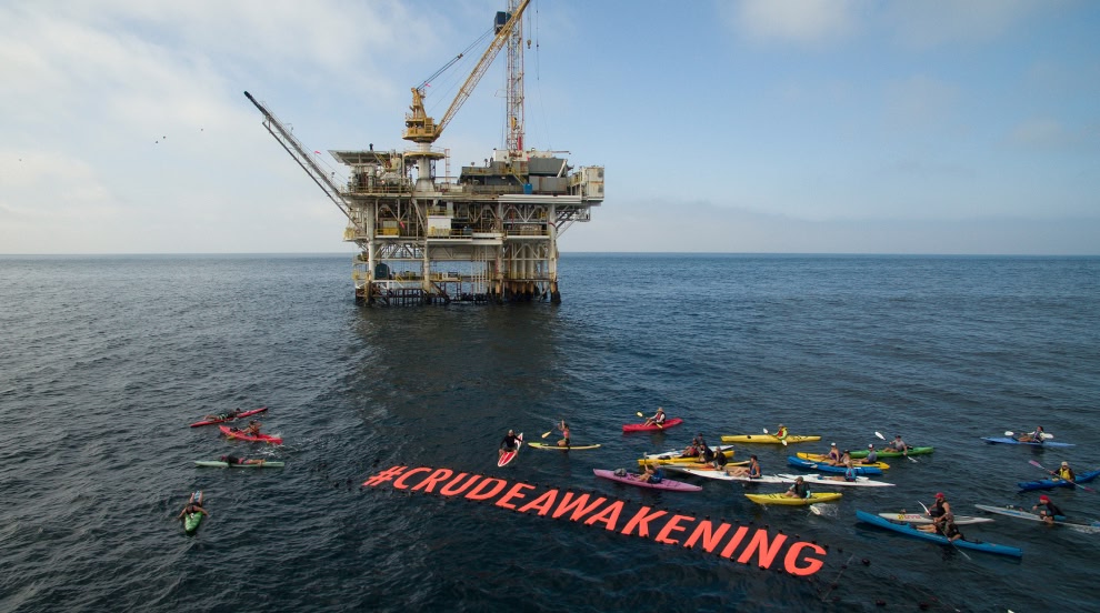 A group of kayakers and paddleboarders float around an offshore oil platform in protest of pollution from oil excavation and transport.
