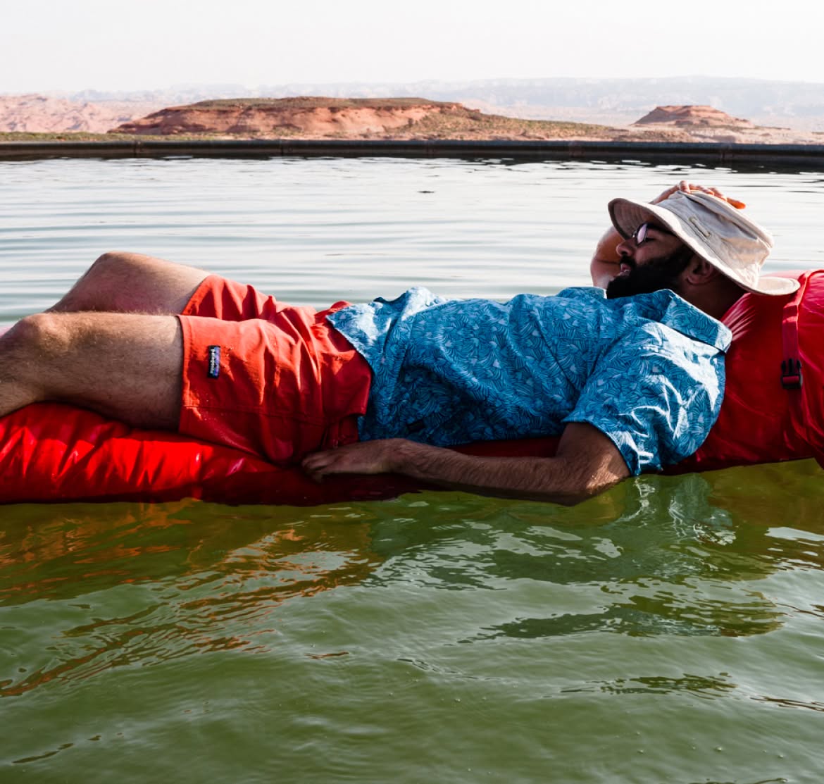 A person lounges on an inflatable raft in a desert lake on a hot day.