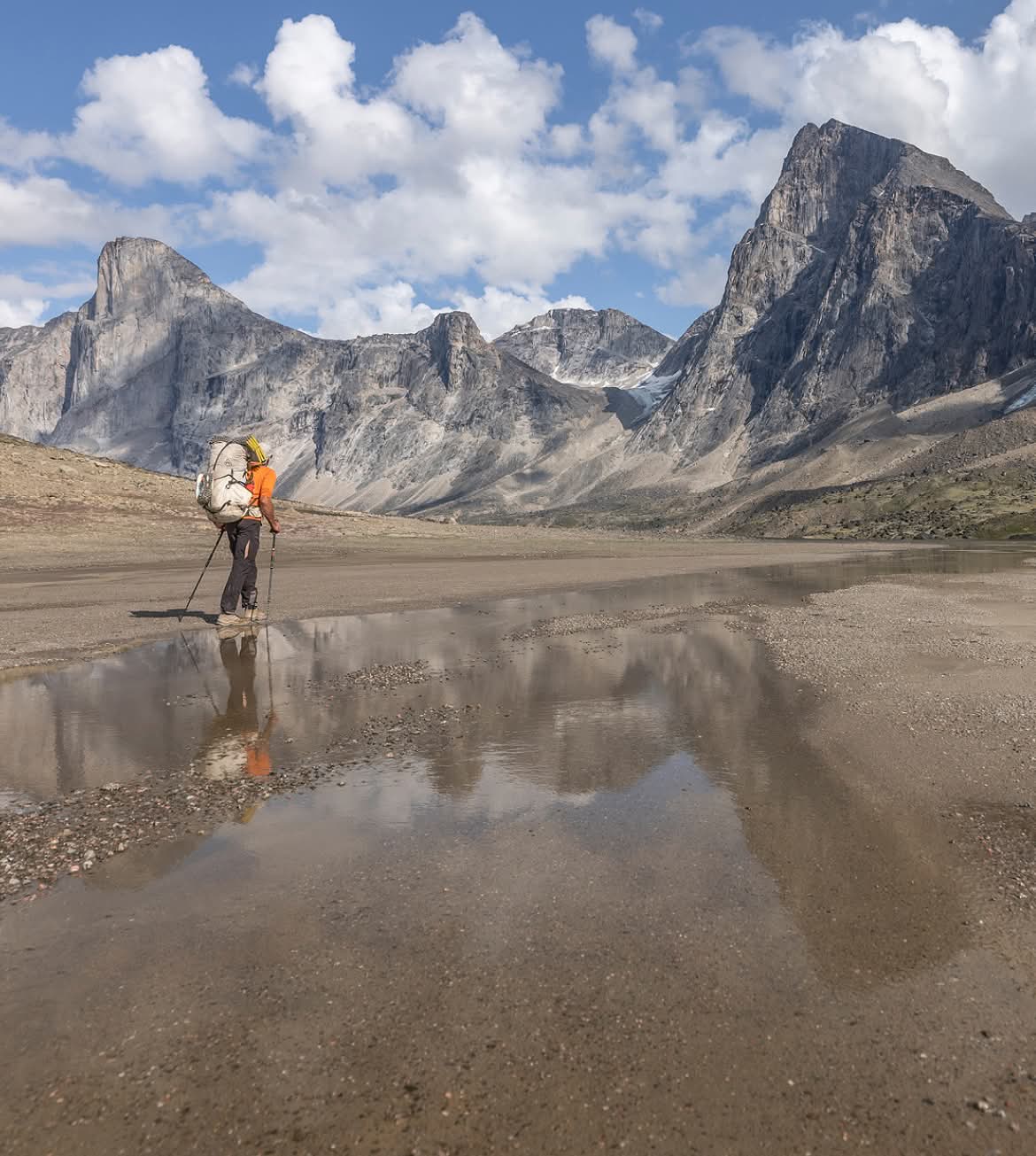 A backpacker hikes along a stream toward granite peaks.