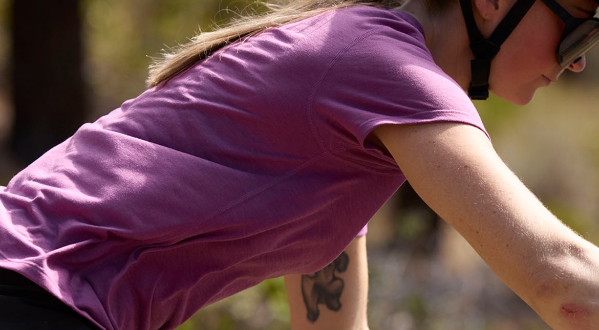 A mountain biker wears a pink shirt, sunglasses and a helmet.