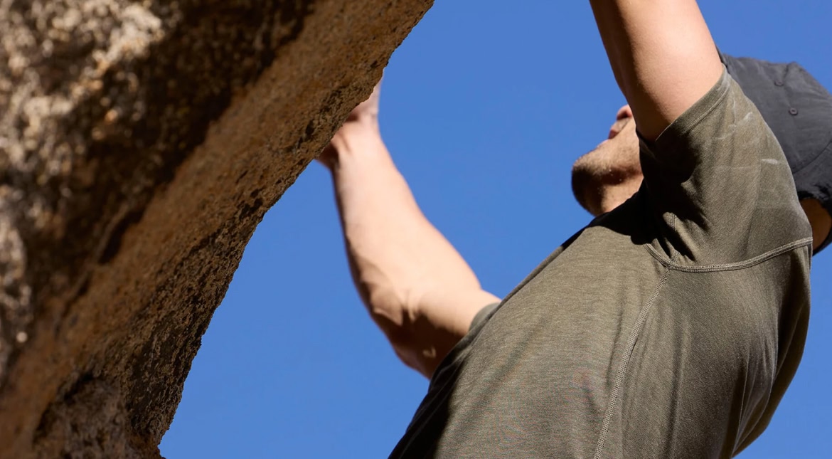 A climber wears a dark green shirt, and a hat.