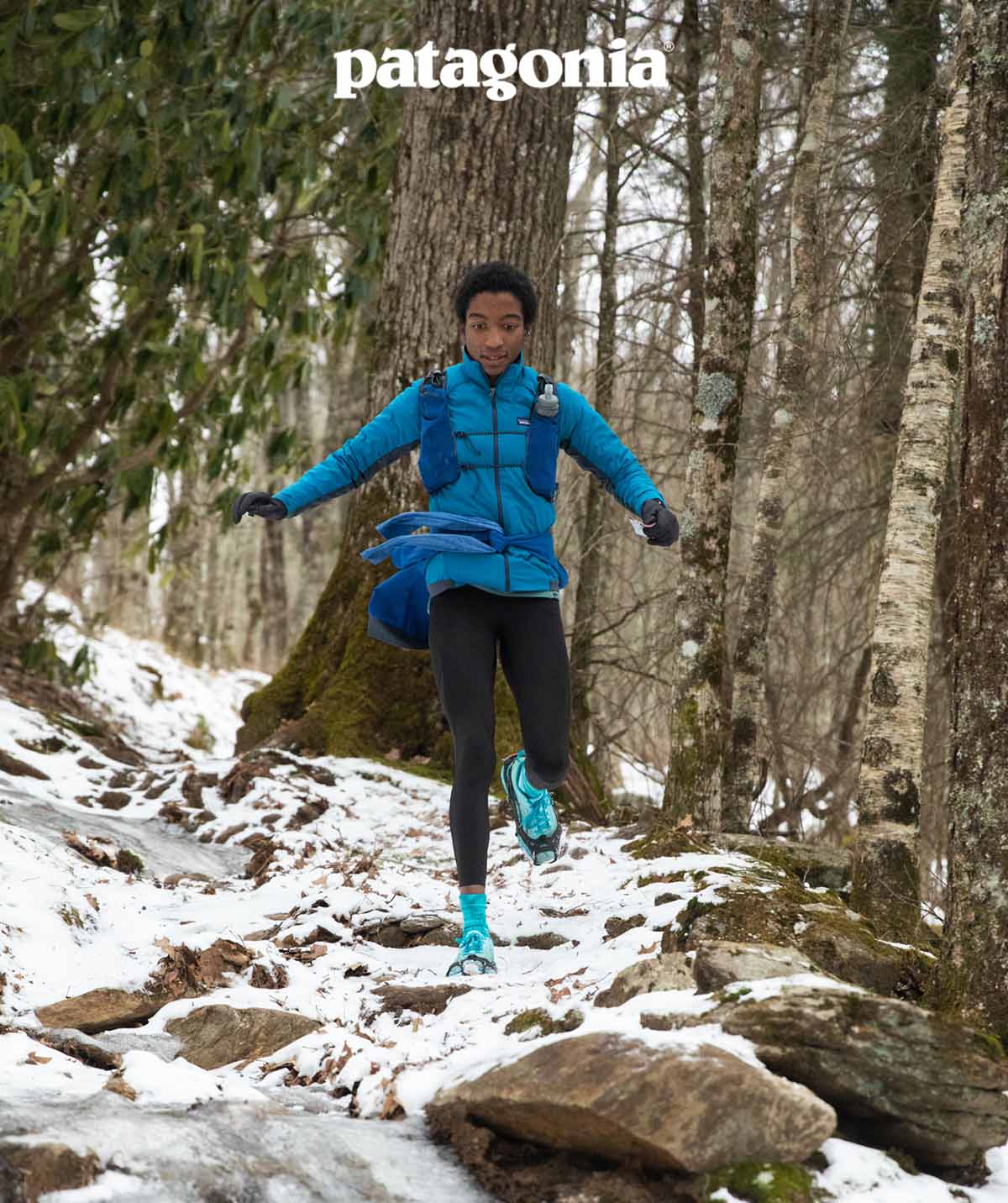 A person jogs down a rocky trail that’s covered in snow