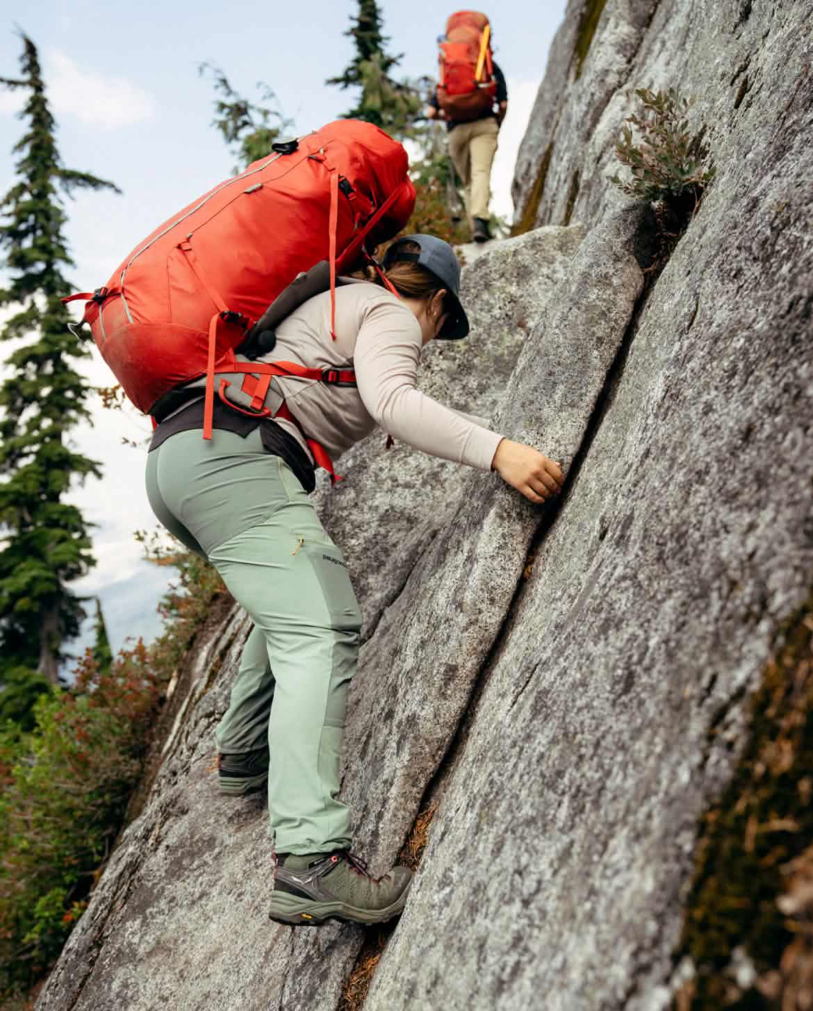 Two people hike climb up a steep granite section of trail.
