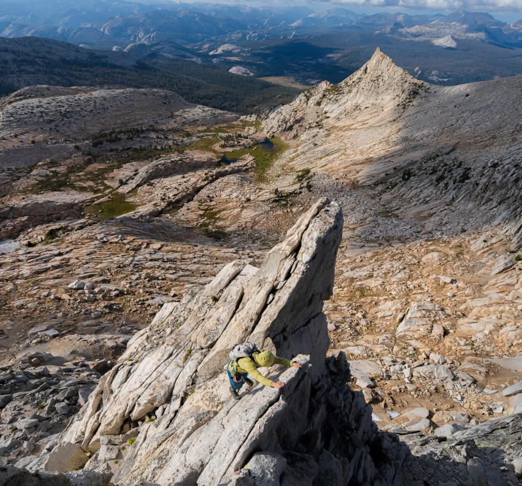 A person summits a craggy peak above tree line.