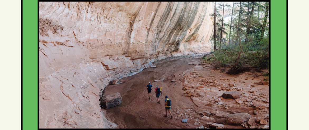 hree people run on a muddy arroyo at the base of a desert canyon.
