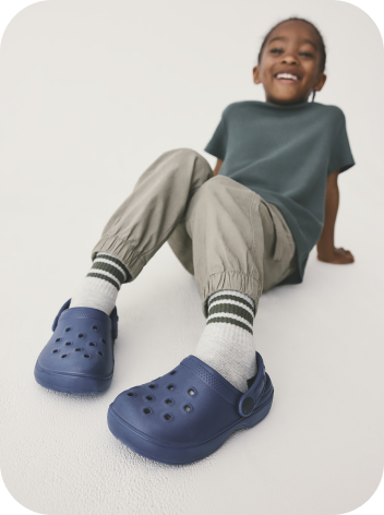 A young boy lounging around in leisurewear and blue shoes