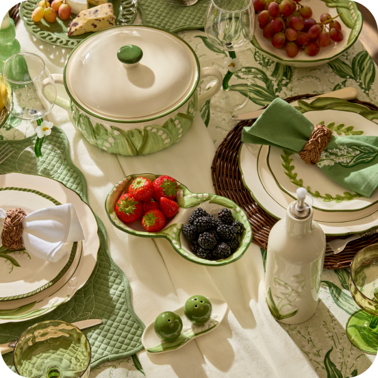 A table with green and white plates, floral cooking pot, strawberries and raspberries in a ceramic dish 