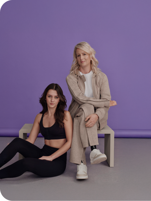 Two ladies, one wearing black co ord gym set sat on the floor and another wearing a beige co ord sat on a chair 