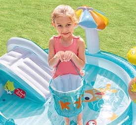 Mädchen in rosa Shirt steht mit aufblasbarem Eimer in aufgeblasenem Planschbecken mit kleiner Rutsche und bunter Dekoration