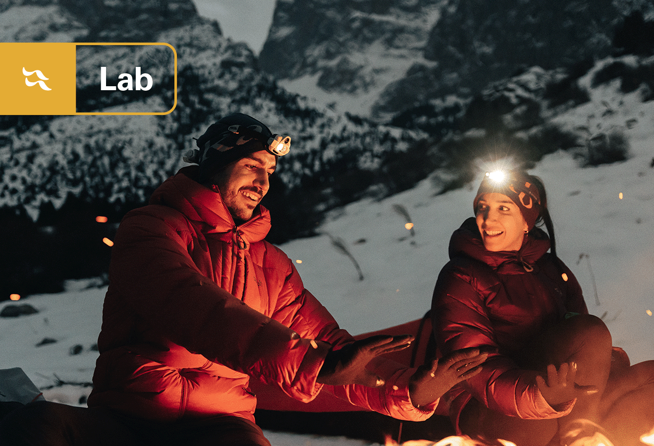 Two alpinist donning a synthetic jackets on a snowy mountainside.