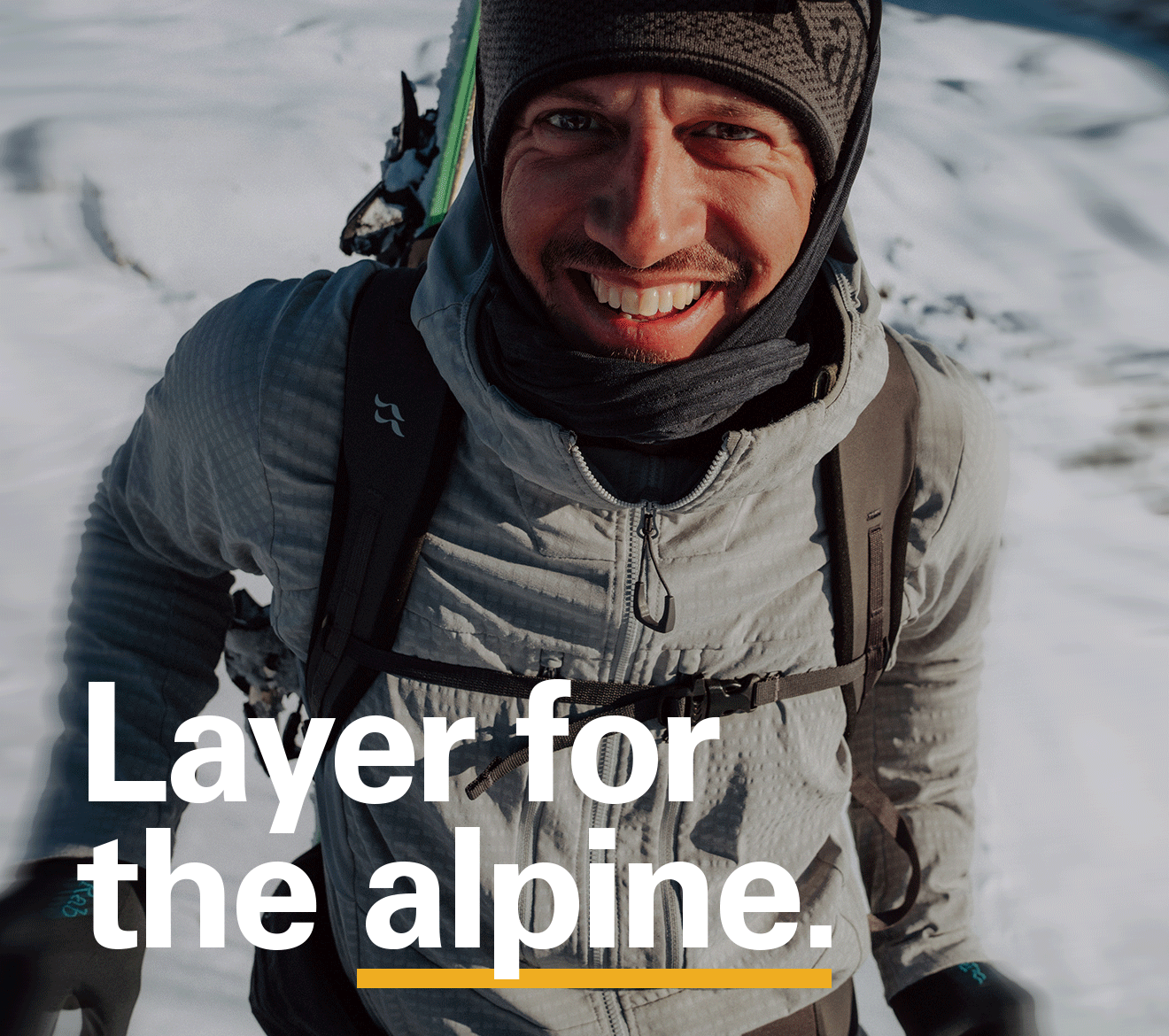 'Layer for the alpine' text over the image of a man up in the mountains smiling.