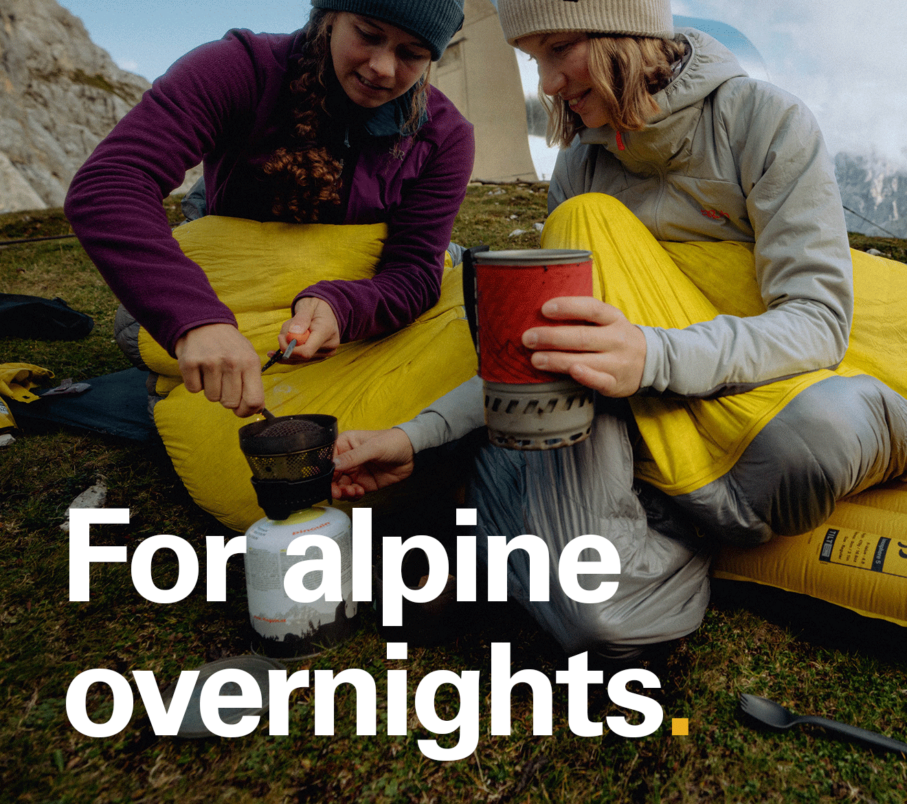 two women wrapped up in sleeping bags cooking food for the night - For alpine overnights