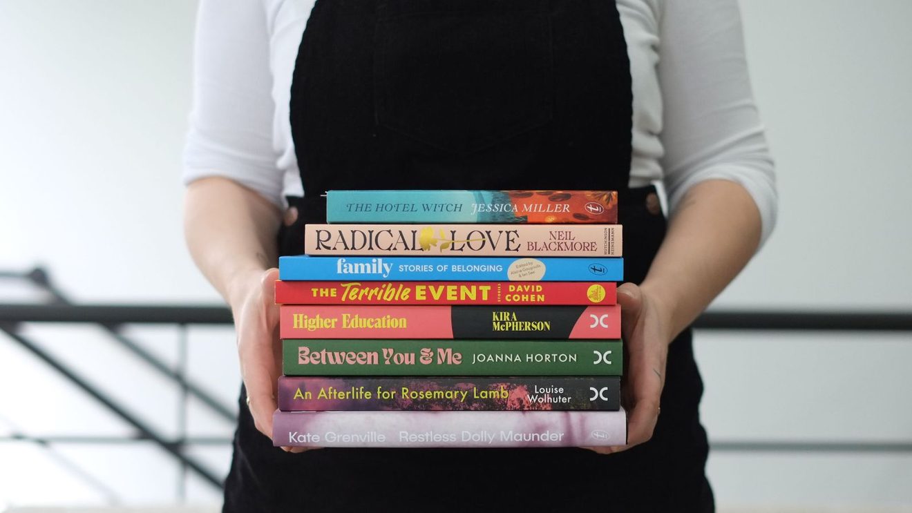 A person holding a stack of books, spines showing.