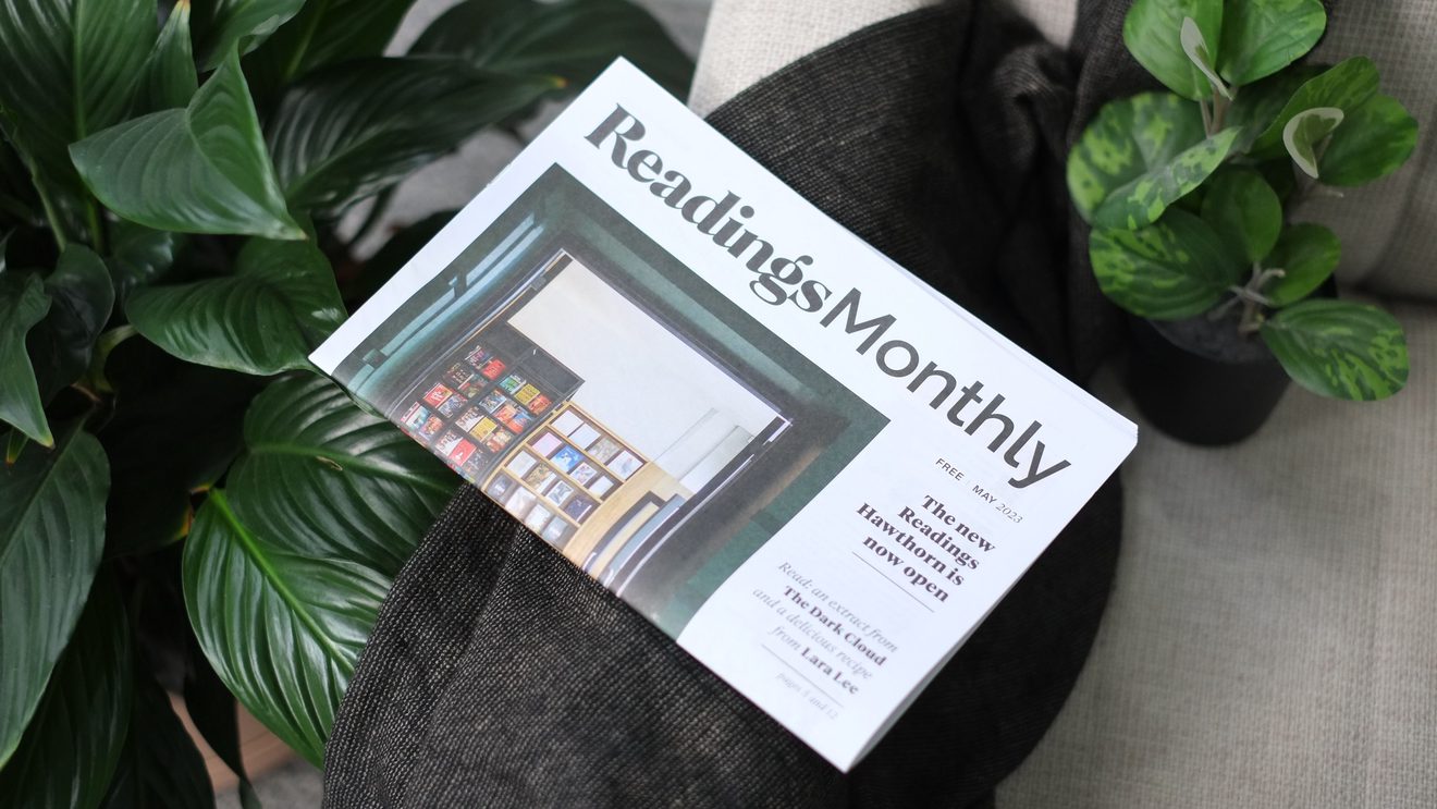 A copy of the Reading Monthly newspaper resting on the arm of a couch, surrounded by houseplant foliage.