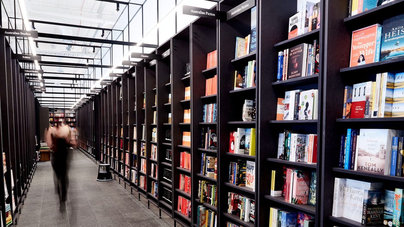 A person walking through ailses of bookshelves at our Emporium shop.