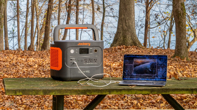 Portable power station powering a laptop, sitting on a picnic table in a campsite. 