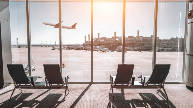 Airport lounge  - four chairs in front of a row of windows and a plane is taking off. 