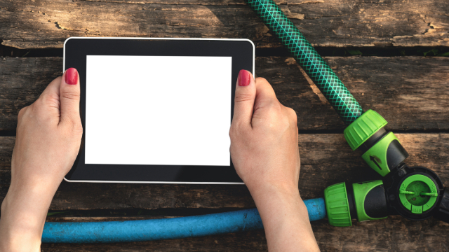 Hands with pink painted fingernails holding a tablet in their hands in the middle of two hoses. One is green, the other blue and a lime green and black connector. 