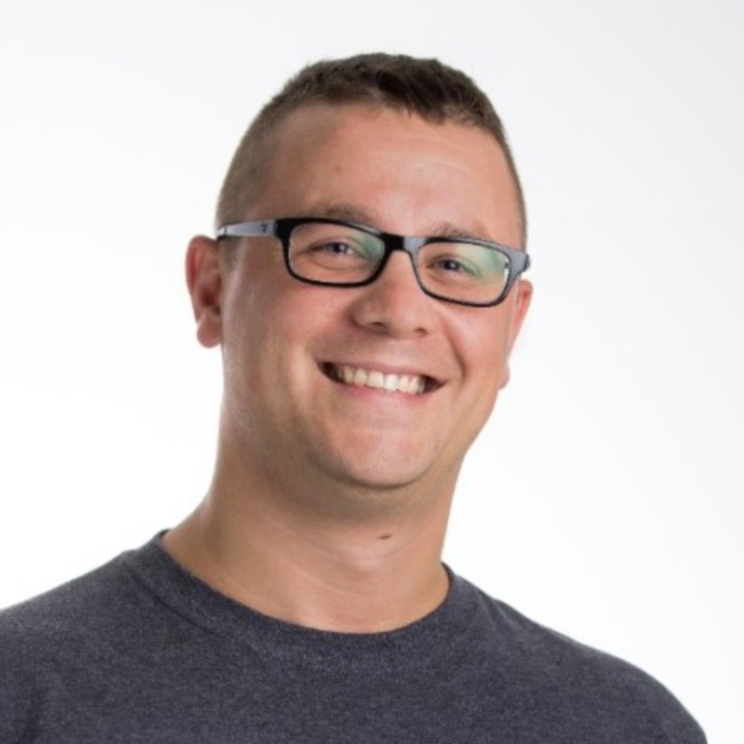 Smiling man wearing glasses and a dark grey T-shirt, headshot portrait on a white background