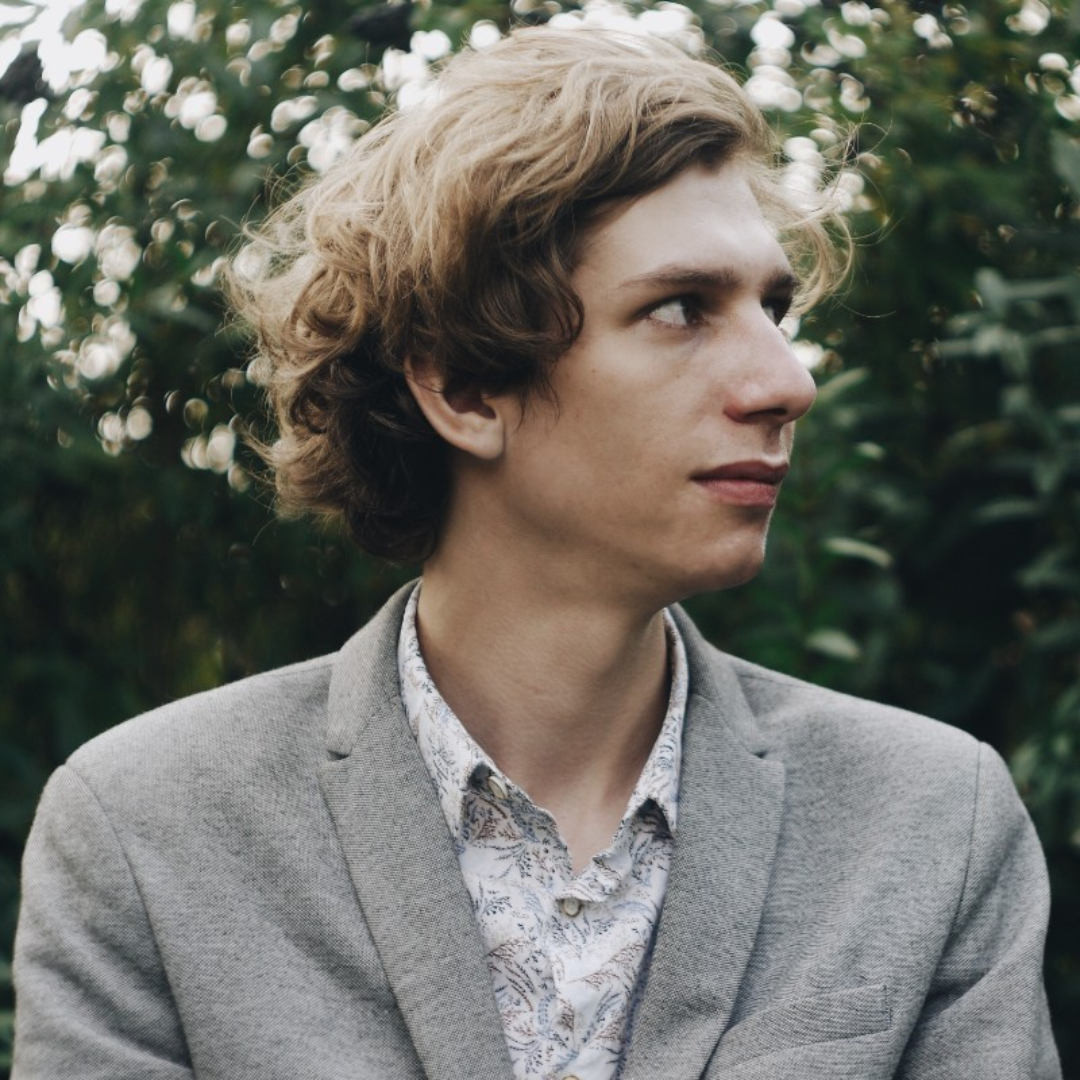 Young man portrait outdoors wearing grey blazer and patterned shirt, curly blond hair, looking to the right