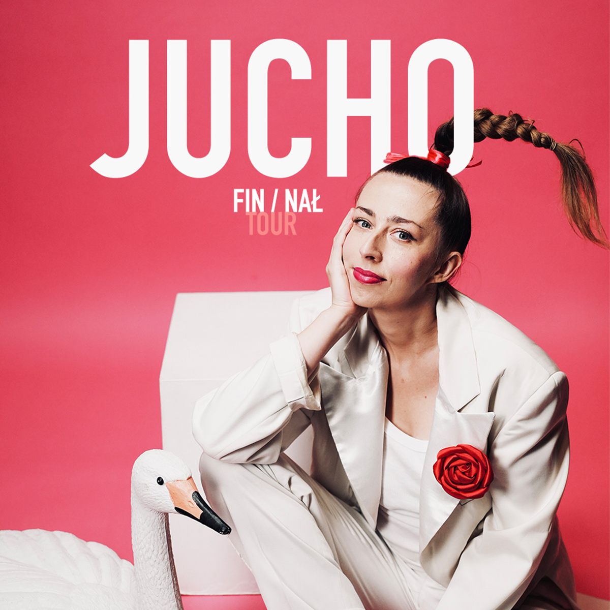 Woman in white suit with braided ponytail and red rose pin seated beside a swan prop on pink background, promotional poster reading 'Jucho'