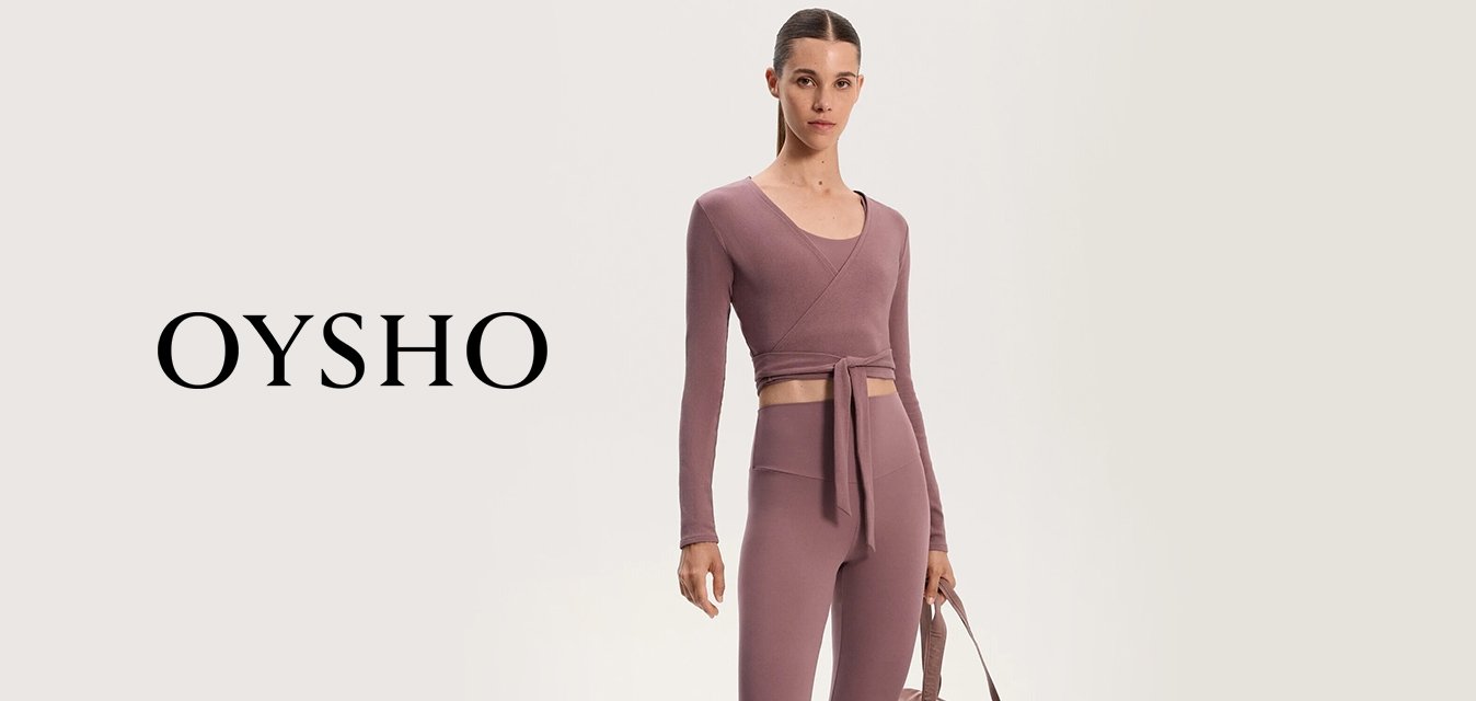 Top corto sportivo in malva con chiusura a fiocco, abbinato a leggings a vita alta; il modello tiene una borsa da viaggio color taupe coordinata; sneakers con dettagli crema.