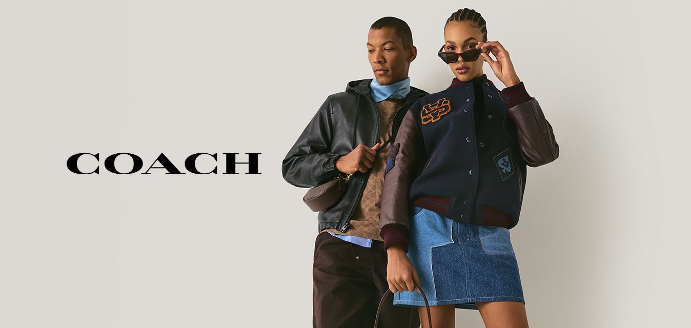 Due modelli posano contro un muro semplice; uno indossa una giacca di pelle, pantaloni marroni e sneaker, l'altro una giacca varsity, una gonna di jeans, stivali e occhiali da sole.