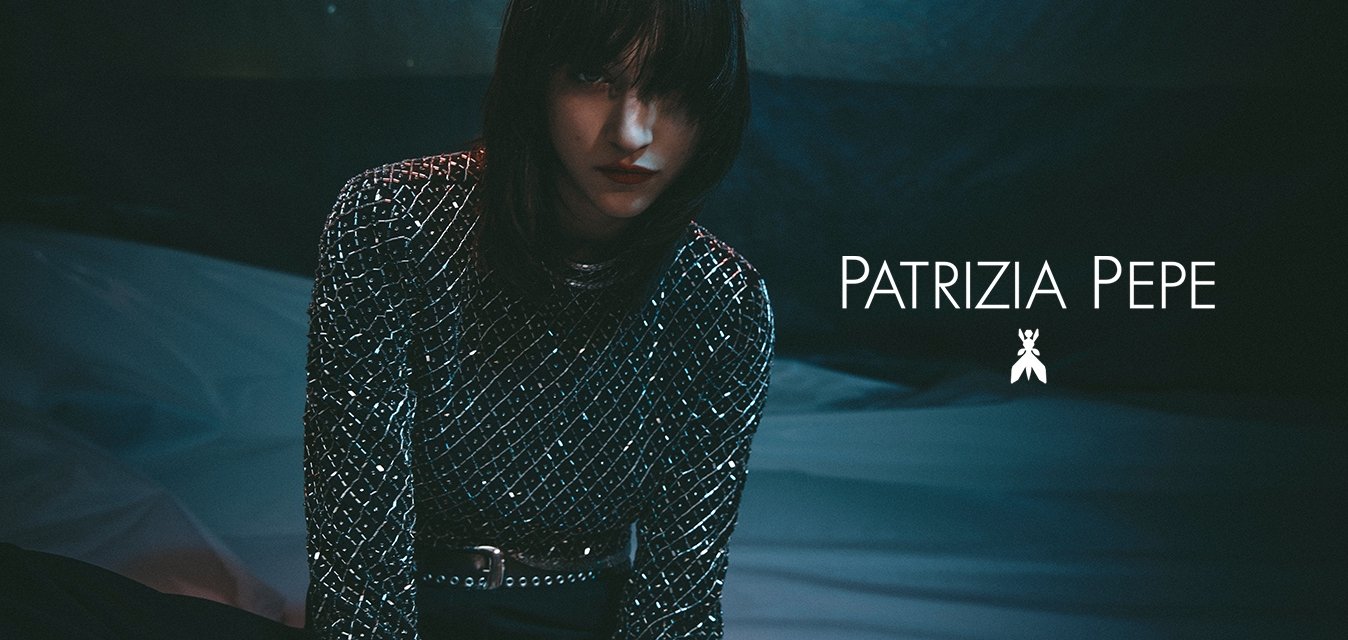 Maglietta a maniche lunghe nera e argento con un motivo a griglia, dotata di paillettes e una cintura metallica, su uno sfondo scuro e strutturato.