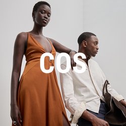 Lungo abito arancione con scollatura profonda e spacco laterale, abbinato a una camicia leggera con texture e pantaloni scuri, impreziosito da una borsa marrone.