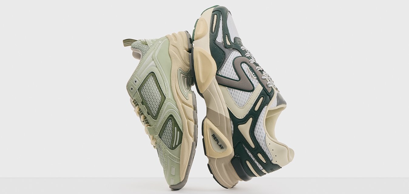 Un paio di sneakers atletiche chunky nei toni beige, verde e bianco, posizionate tallone contro tallone su una superficie bianca davanti a uno sfondo semplice.