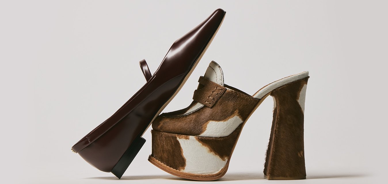 Scarpa mocassino in pelle marrone appoggiata contro un mule in pelle di mucca marrone e bianca con tacco alto a blocco su uno sfondo bianco.