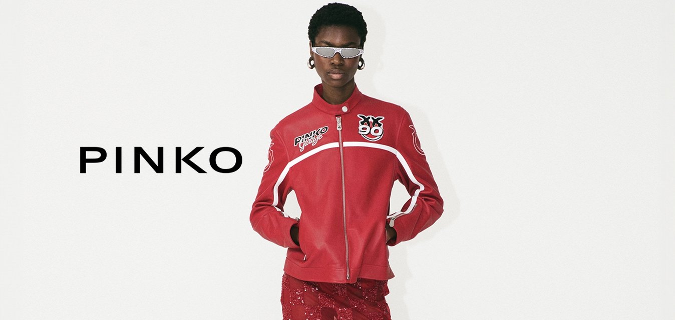 Giacca rossa con zip e dettagli con logo, abbinata a una gonna midi rossa in pizzo con motivo a scacchi e sandali bianchi con tacco.