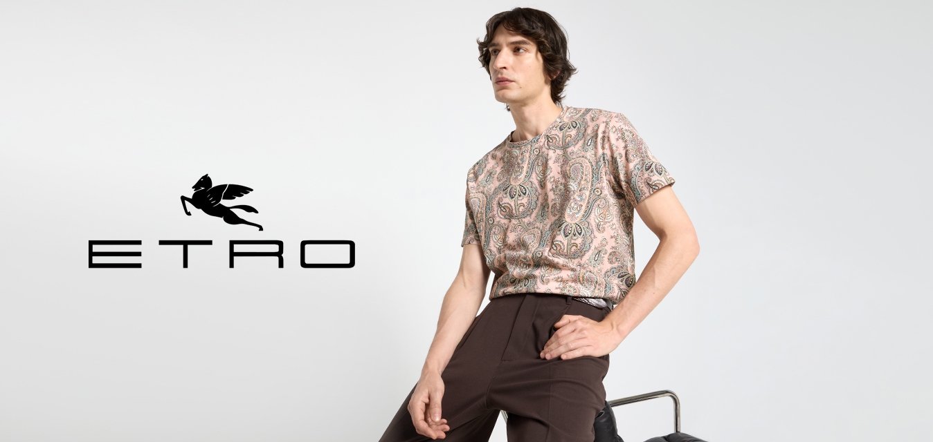 Camicia a maniche corte con motivo paisley in rosa, caratterizzata da un collo rotondo, indossata con pantaloni marroni scuri. Tessuto morbido con vestibilità rilassata.