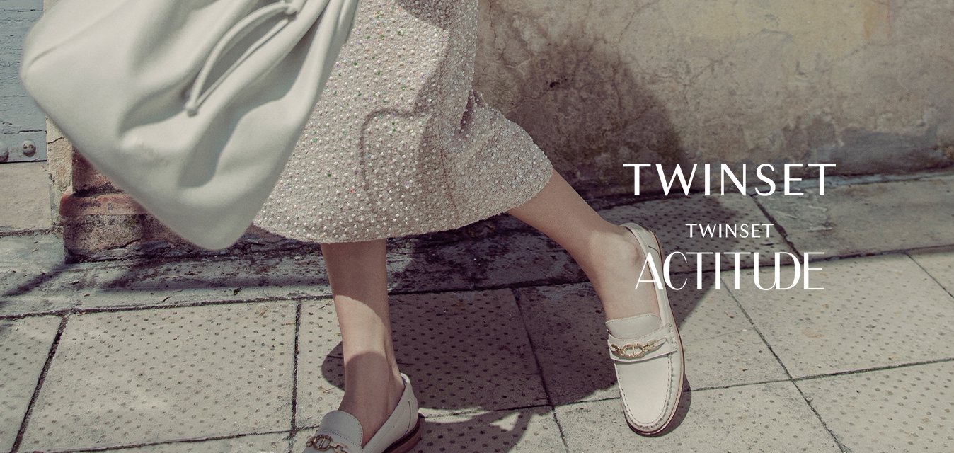 Camicia bianca con maniche ricamate, gonna con fantasia, borsa leggera e mocassini con un dettaglio decorativo. Texture morbide, colori chiari.