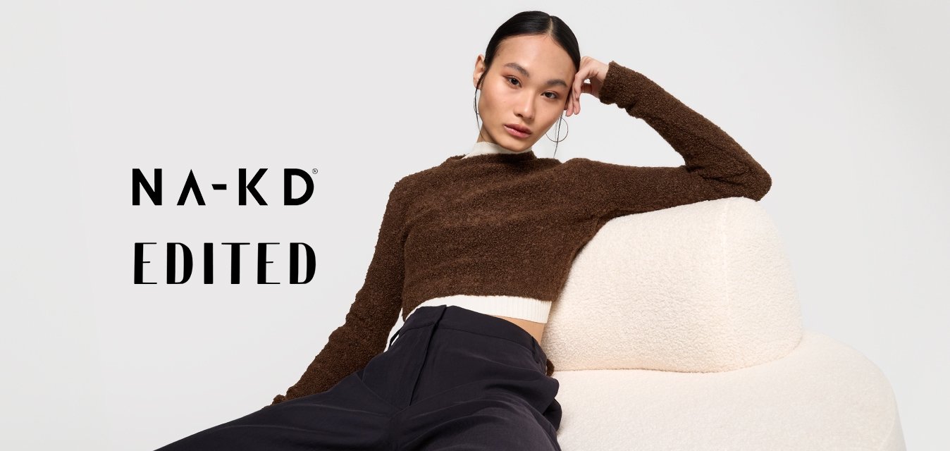 Maglione corto marrone, textured con colletto bianco, indossato con pantaloni larghi blu navy, seduto su un divano rotondo, soffice di colore avorio.